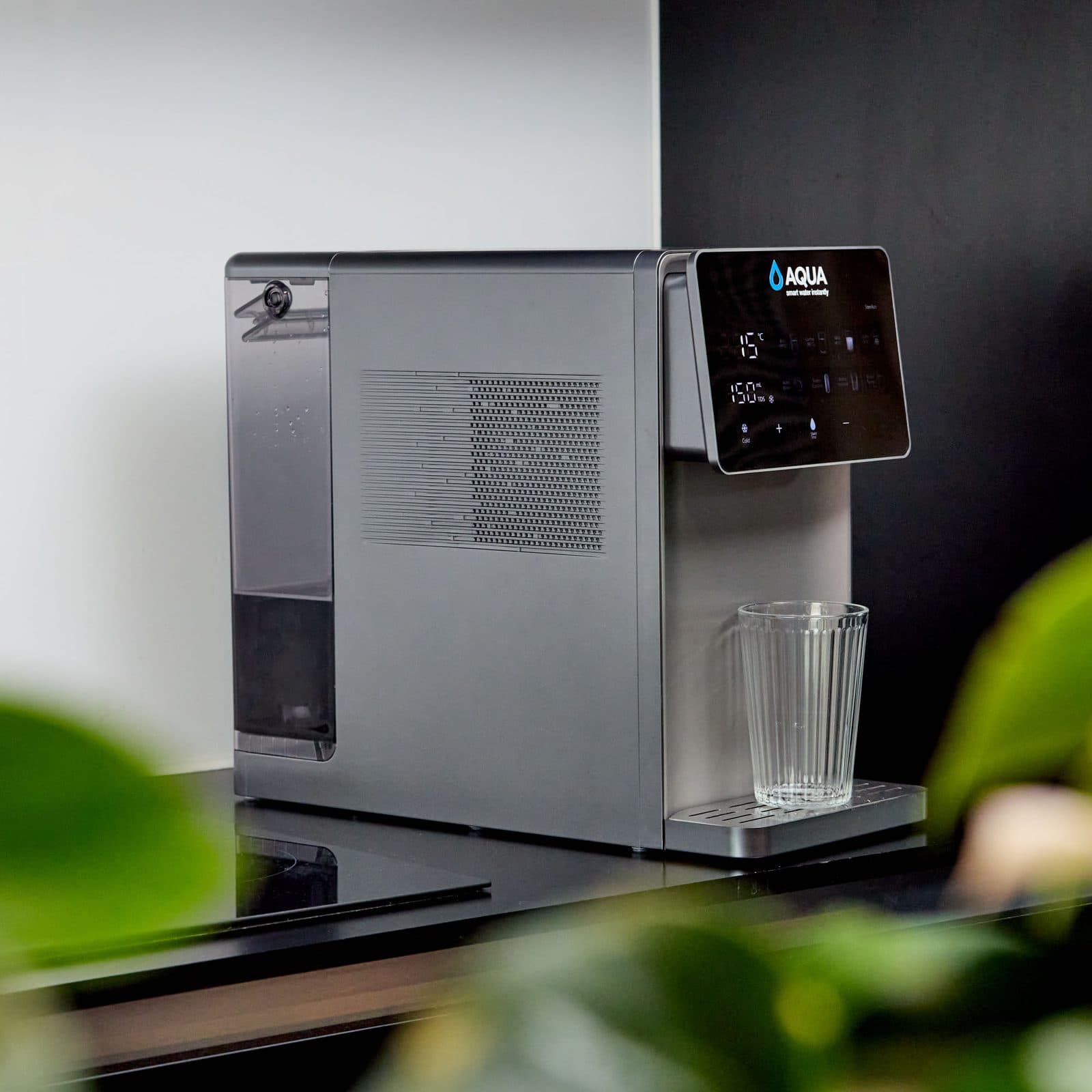 The Aqua dispenser on a kitchen counter with a glass of water